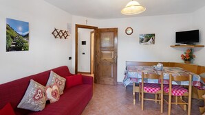 Ein gemütliches Zimmer mit einem roten Sofa, einem Holzesstisch, Stühlen, einem Fernseher und einer Tür zu einem anderen Raum.