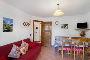 A cozy room with a red sofa, wooden dining table, chairs, a television, and a door leading to another room. - Apartment 'Chalet Sever' with Wi-Fi (Livigno)