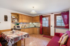 A compact kitchen with wooden cabinets, a dining table with a quilt, a microwave, and a window with red curtains. - Apartment 'Chalet Sever' with Wi-Fi (Livigno)