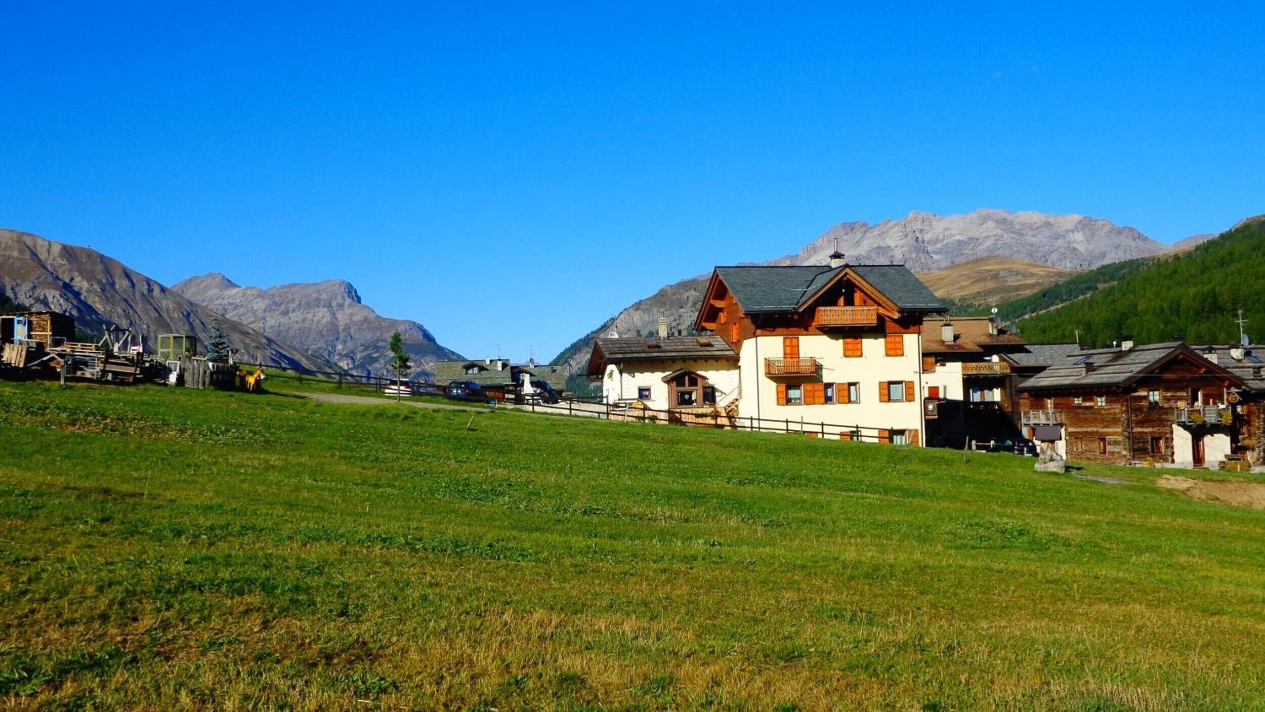 Uma vila de montanha com casas de madeira tradicionais, céu claro e um campo gramado.