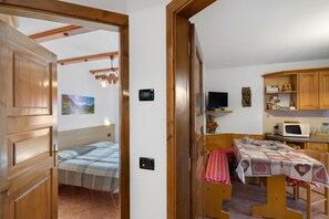 Una habitación pequeña con cama, una mesa con mantel, microondas, televisor y armarios de madera.