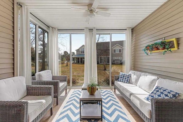 A covered patio with wicker furniture, a central table, and a view of the backyard. - Sea Colony Condo with Fast WiFi & Gas Fireplace plus Shared Pools, Hot Tub, Gym (Bethany Beach)