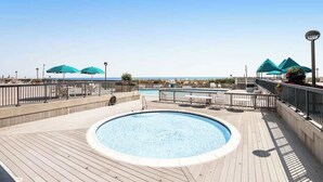 En pool på taket med utsikt över havet, omgiven av parasoller och solstolar.