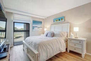 A bedroom with a bed, bedside tables, a TV, and a view of the outdoors. - 2nd Floor Condo with Balcony, Shared Pool/HT/Tennis, AC (Bethany Beach)