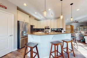 A modern kitchen with a central island, bar stools, stainless steel appliances, and pendant lighting. - Bayside Resort condo - fireplace, central AC & private W/D - pools, gym & golf (Selbyville)