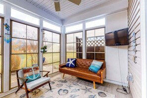 Un solarium con ventanas amplias, un sofá de cuero, una silla y un televisor.
