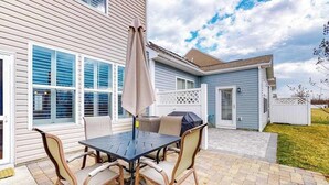 Une terrasse avec une table et des chaises, un barbecue et un parasol.