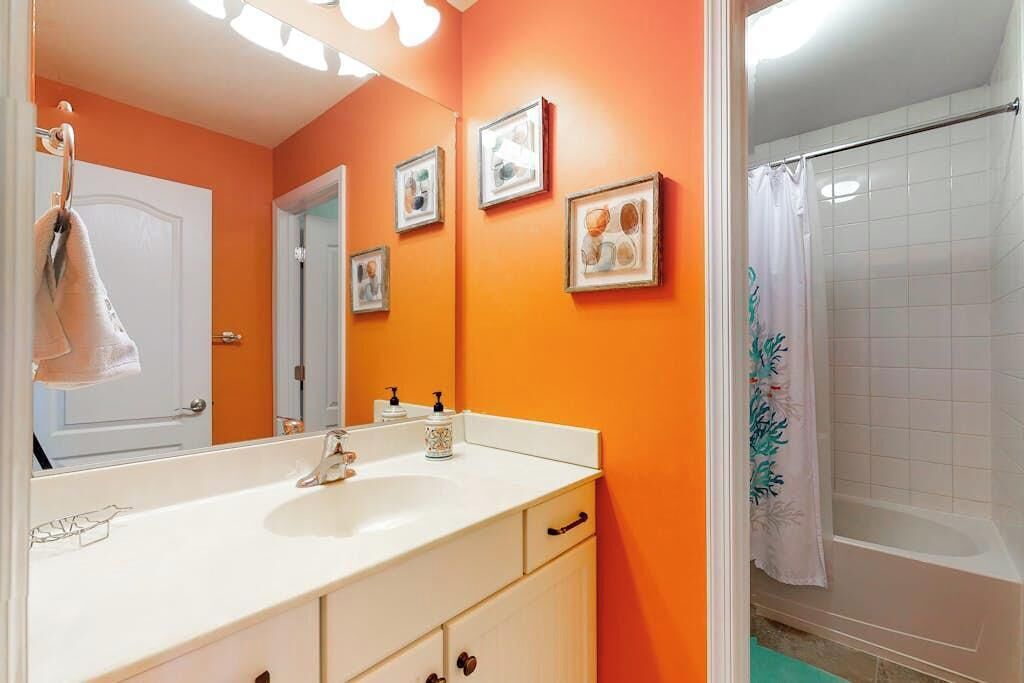 A bathroom with an orange wall, a white sink, and a shower area.