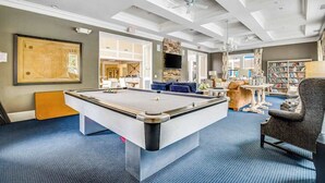 Une table de billard dans une pièce dotée d’un ventilateur de plafond, d’une bibliothèque et d’un coin salon.