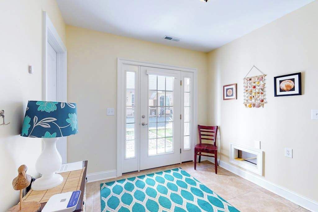 A room with a white door, a patterned rug, a wooden chair, and wall-mounted decor.