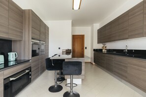 A modern kitchen with built-in appliances, a central island with bar stools, and a wooden door in the background. - Cascais Golden Horizon By Clama Retreats (Cascais)