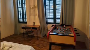 A room with a foosball table, a desk, a chair, and a bed.