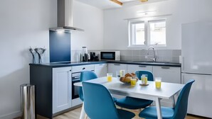 A modern kitchen with white cabinets, a stainless steel range hood, a microwave, and a dining area with a white table and blue chairs.