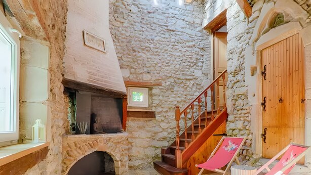 A stone interior with a fireplace, wooden staircase, and a wooden door.