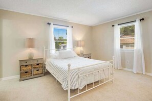 A bedroom with a bed, bedside tables, a window with curtains, and a view of the outdoors. - Bright Turtle Walk escape near the beach & town with screened porch, grill & AC (Bethany Beach)