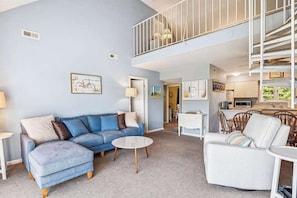Ein Wohnzimmer mit einem blauen Sofa, einem weißen Sessel, einem Couchtisch und einer Treppe, die zu einer oberen Ebene führt.