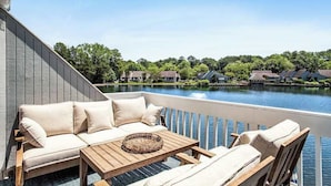 Un balcon agrémenté d’un canapé, de chaises et d’une table, d’où l’on peut admirer un lac avec des maisons en arrière-plan.