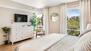 Une chambre à coucher avec un lit, une commode, une télévision, un miroir et une fenêtre donnant sur un beau paysage.