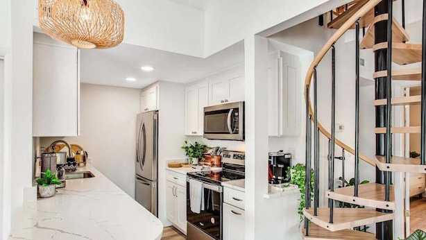 Une cuisine moderne avec des meubles blancs, des appareils en acier inoxydable, un comptoir en marbre et un escalier en colimaçon en bois.