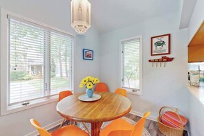 A dining area with a round wooden table, orange chairs, a vase with yellow flowers, and a hanging light fixture. - Stewards Watch townhome near beach with screened porch, pool & tennis access (Bethany Beach)