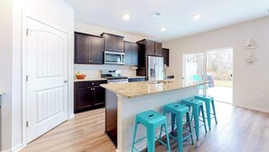 A modern kitchen with dark cabinets, a central island with bar stools, and a large window. - Ocean View Beach Club home with fast WiFi, central A/C, & community amenities (Ocean View)
