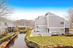 A modern two-story house with a small front yard, a visible outdoor unit, and a narrow water channel. - East of the Sun condo w/ central AC, W/D, & shared pool - under 1 mile to beach (Fenwick Island)