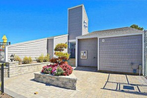 A building with a brick facade, a garage door, and a landscaped area with flowers. - East of the Sun condo w/ central AC, W/D, & shared pool - under 1 mile to beach (Fenwick Island)