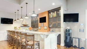 Una cucina moderna con isola centrale, sgabelli da bar, illuminazione a sospensione, televisore integrato e dispenser d'acqua.