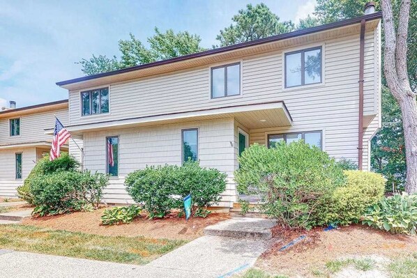 A two-story apartment building with a front porch, a flag, and well-maintained landscaping. - Bethany Pines townhome with pool, tennis, & private washer/dryer - near beach (Bethany Beach)