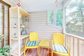 Ein Balkon mit zwei gelben Stühlen, einem kleinen Tisch und einem weißen Regal mit verschiedenen Gegenständen.