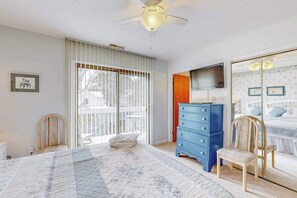 A bedroom with a large bed, a blue dresser, a chair, a ceiling fan, and a TV on the wall. - Bethany Pines townhome with pool, tennis, & private washer/dryer - near beach (Bethany Beach)
