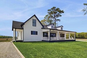A two-story house with a covered porch and a gravel driveway. - Fully renovated ranch home with large patio and firepit (Dagsboro)