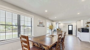 A spacious dining area with a wooden table and chairs, large windows with blinds, and a view of the outdoors. - Fully renovated ranch home with large patio and firepit (Dagsboro)
