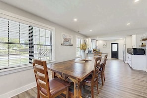 A spacious dining area with a wooden table and chairs, large windows with blinds, and a view of the outdoors. - Fully renovated ranch home with large patio and firepit (Dagsboro)