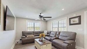 A living room with a sectional sofa, a coffee table, a ceiling fan, and large windows. - Fully renovated ranch home with large patio and firepit (Dagsboro)