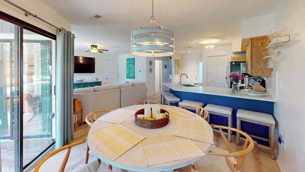 A modern kitchen with a central island, a dining area with a round table, and a living space with a sofa and TV.