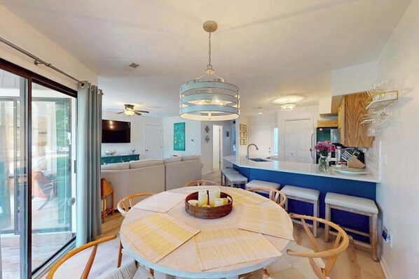 A modern kitchen with a central island, a dining area with a round table, and a living space with a sofa and TV. - East of Sun condo with water-view patio, on-site pool & tennis - near beach (Fenwick Island)
