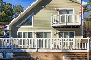 A two-story house with a balcony, a flag, and a porch with a railing. - South Bethany cottage with private pool, firepit, & more - 5 minutes from beach (South Bethany)