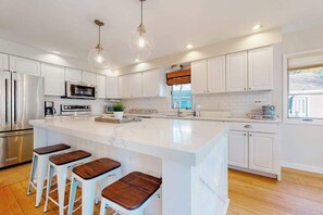 A modern kitchen with white cabinetry, stainless steel appliances, and a large island with bar stools. - South Bethany cottage with private pool, firepit, & more - 5 minutes from beach (South Bethany)