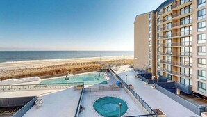 Um hotel com piscina no terraço e vista para a praia, um edifício de vários andares com varandas, e uma vista ampla do oceano.