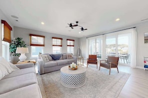 A modern living room with a grey sofa, a round coffee table, a brown leather chair, and a ceiling fan. - Tidal Walk home with pond views, outdoor pool, decks, fast WiFi, & bikes (Ocean View)