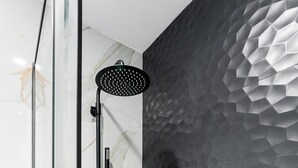 A modern bathroom with a glass shower enclosure, a handheld showerhead, and a textured wall. - GuestReady - Studio in Cedofeita (Porto)