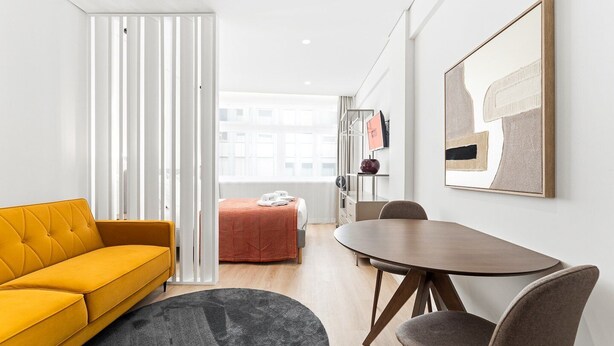 A modern hotel room with a yellow sofa, a dining table with chairs, a bed with a red blanket, and a large framed artwork on the wall. - GuestReady - Studio in Cedofeita (Porto)
