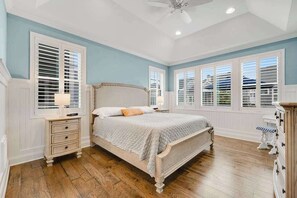 Une chambre à coucher comprenant un lit, des tables de chevet, une commode et un ventilateur de plafond.