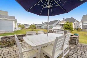 Une terrasse avec une table et des chaises, un parasol et un barbecue.