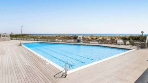 A rectangular swimming pool with a wooden deck, surrounded by a low fence, and overlooking a beach with dunes. - Sea Colony oceanfront condo with private balcony, shared pools, & gym (Bethany Beach)