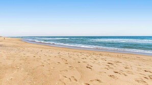 A sandy beach with footprints leading to the water, a clear sky, and a calm sea. - Sea Colony oceanfront condo with private balcony, shared pools, & gym (Bethany Beach)