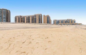 Un hôtel situé en bord de mer, composé de plusieurs immeubles de grande hauteur, avec une plage de sable fin et un ciel dégagé.