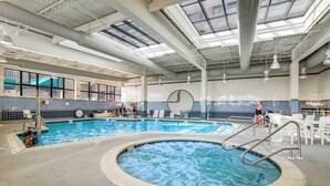 An indoor swimming pool with a hot tub, lounge chairs, and a large windowed wall. - Sea Colony condo with pools, hot tub, tennis, gym, & private deck (Bethany Beach)
