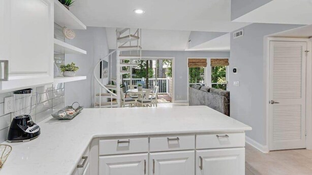 A kitchen with white cabinets, a white countertop, and a spiral staircase leading to a balcony. - Sea Colony condo with pools, hot tub, tennis, gym, & private deck (Bethany Beach)